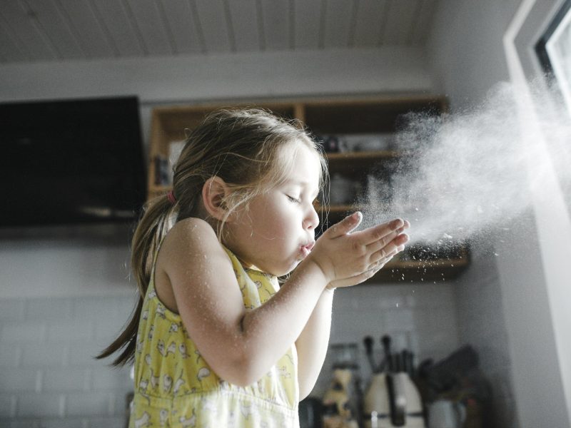 Little girl blowing flour in the air in the kitchen